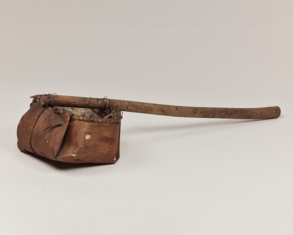 A ladle made from folded bark with a long wooden handle.