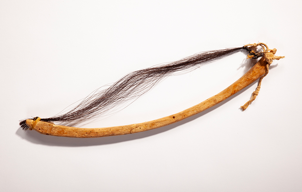 A small wooden bow with a loose string made of dark horse hair that has become unfurled.