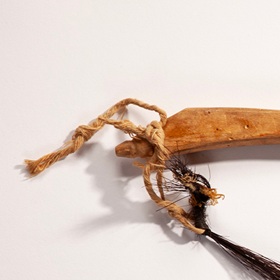 A closeup of the end of a wooden bow with mess of knotted twine connected to slightly loose dark horsehair.