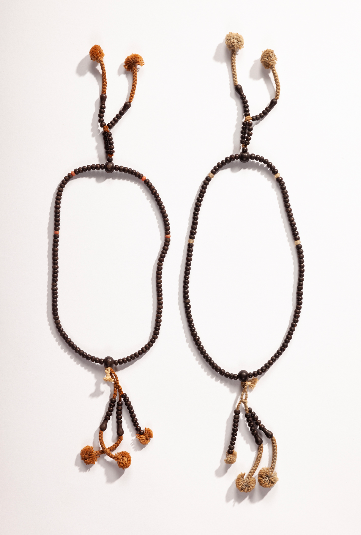 Two beaded rosaries made of dark brown wood with two tassels on the top end and three on the bottom.