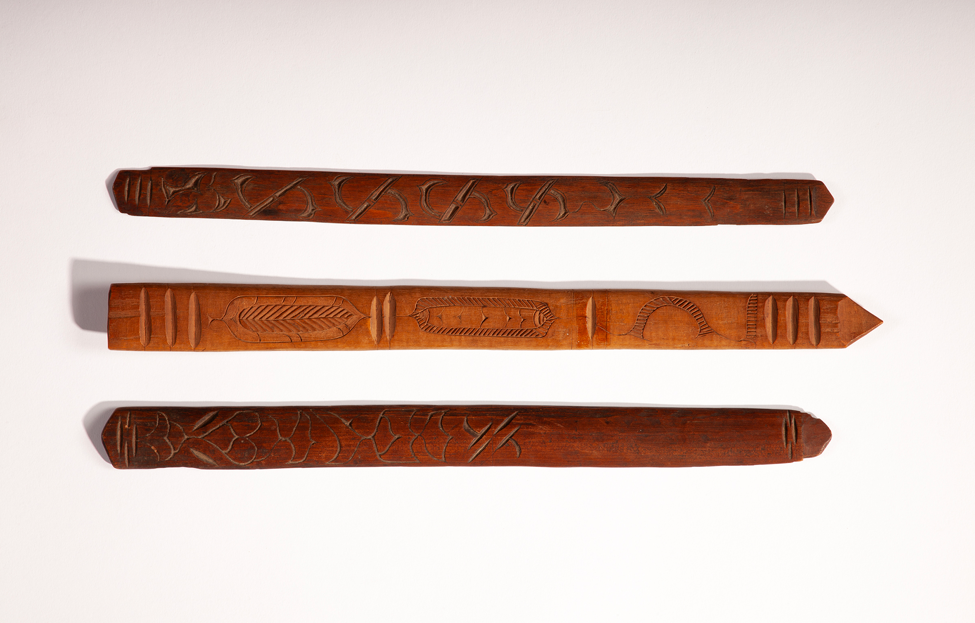 Three long strips of wood of different shades carved with intricate patterns and lined up horizontally on above one another.