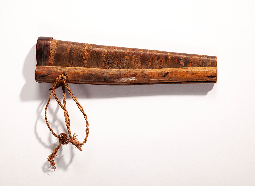 A wooden knife holder of a rich brown color. it has a twisted piece of twine descending from one side.