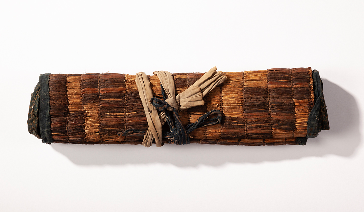 An aged mat rolled up and tied closed with fabric.