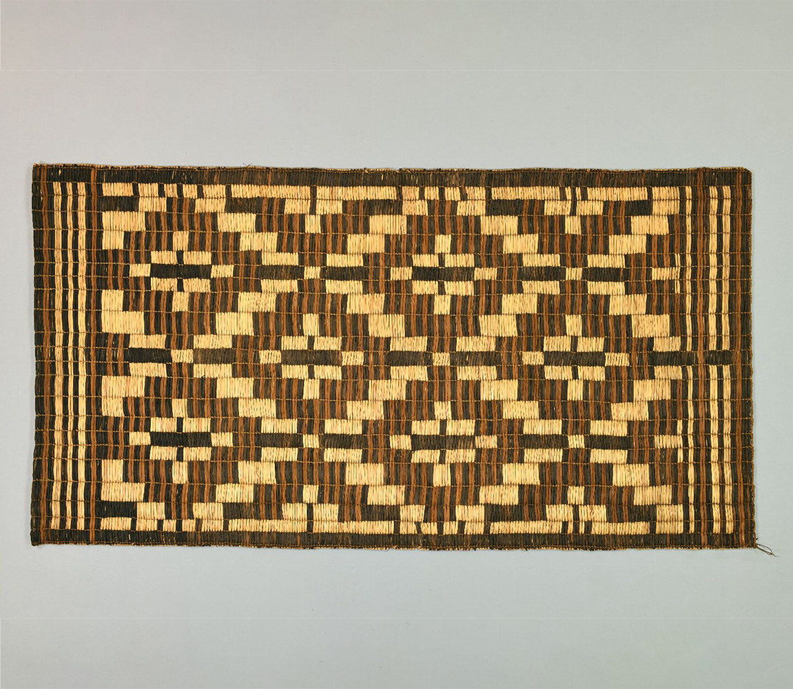 A geometric patterned mat made of cattails in shades of tan, brown, and black resembling diamond shapes.