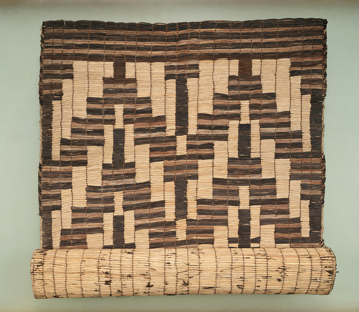 A geometric patterned mat made of cattails in shades of tan, brown, and black.
