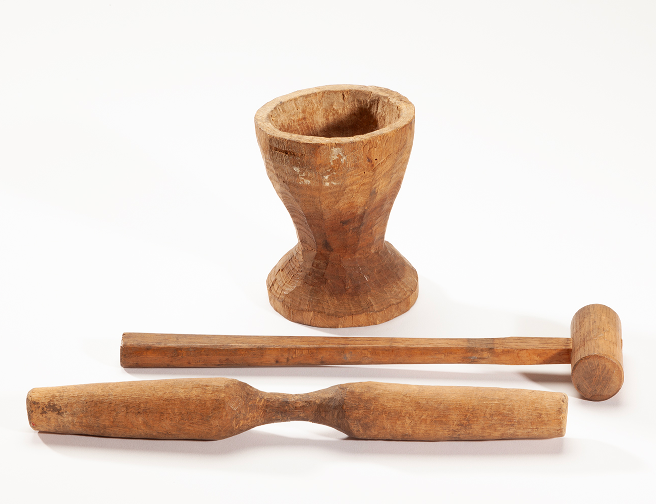 A photograph of three small wooden items, a mortar, pestle, and hammer.