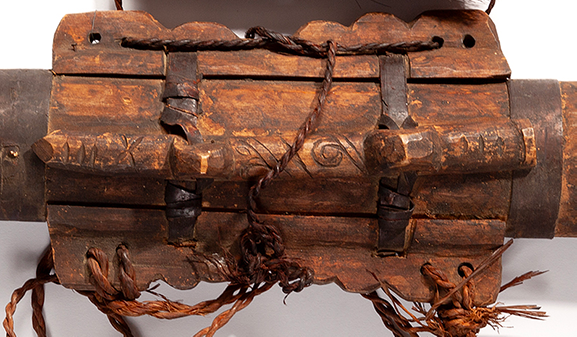 The back of a wooden Ainu quiver with a long carved piece attached to it that is covered in curved carved symbols.